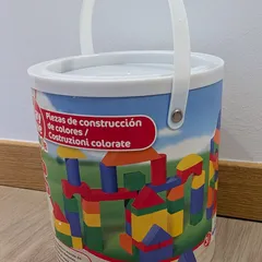 Un cubo con asa lleno de piezas de construcción de madera de colores, con el castillo que se puede montar dibujado en la etiqueta