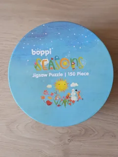 La lata redonda del puzzle Seasons de boppi, de 150 piezas, sobre una mesa de madera