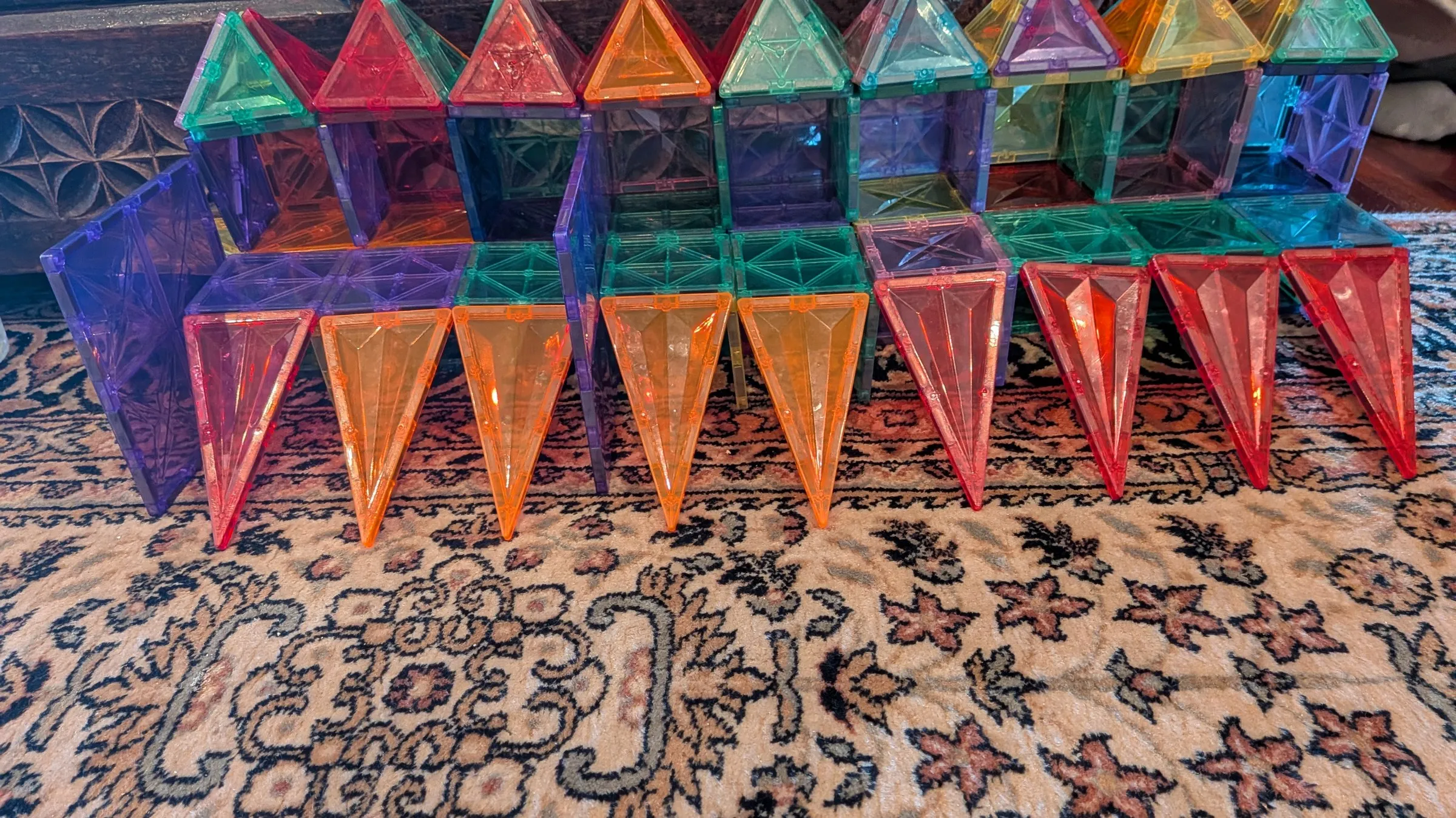 Una muralla larga construida con piezas magnéticas de colores translúcidos, con torres y tejados triangulares, sobre una alfombra