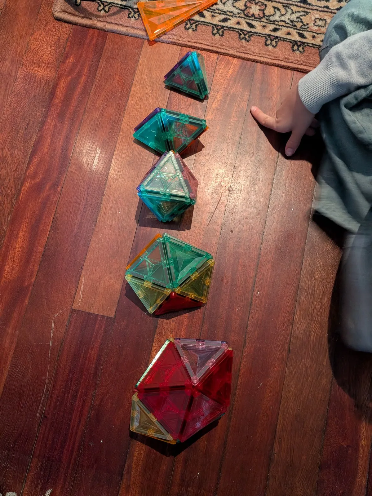 Cinco poliedros de distintos tamaños construidos con piezas magnéticas triangulares, alineados en el suelo de madera