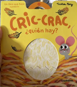 Una mano sostiene el libro Cric-crac, ¿quién hay?, con el pollito saliendo del huevo en la portada y el ratón asomando