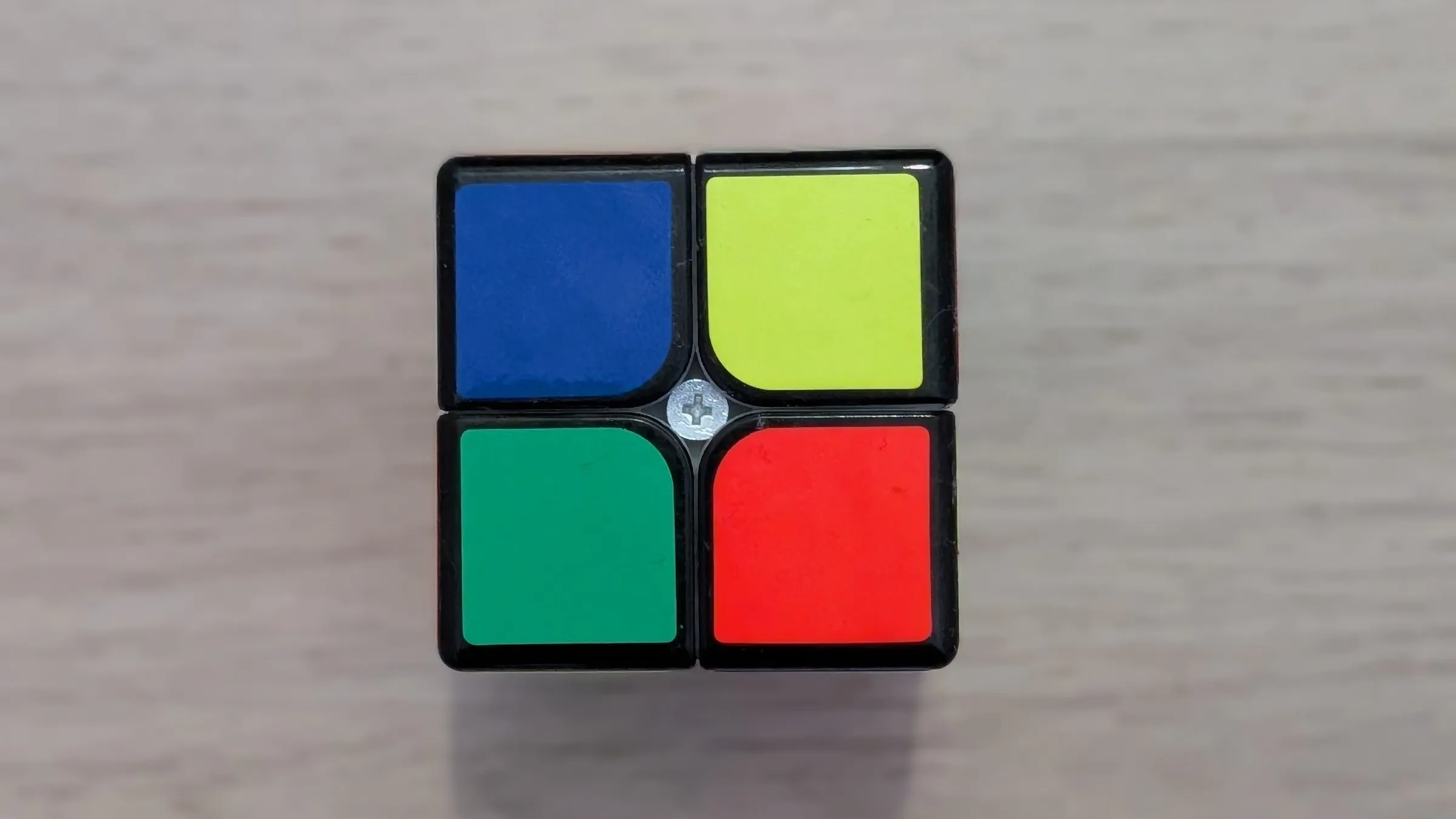 La cara de un cubo de Rubik de 2x2 con los cuatro cuadros de colores distintos, vista desde arriba sobre el suelo de madera
