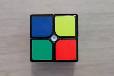 La cara de un cubo de Rubik de 2x2 con los cuatro cuadros de colores distintos, vista desde arriba sobre el suelo de madera