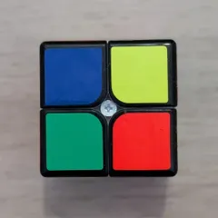 La cara de un cubo de Rubik de 2x2 con los cuatro cuadros desordenados, vista desde arriba sobre el suelo de madera