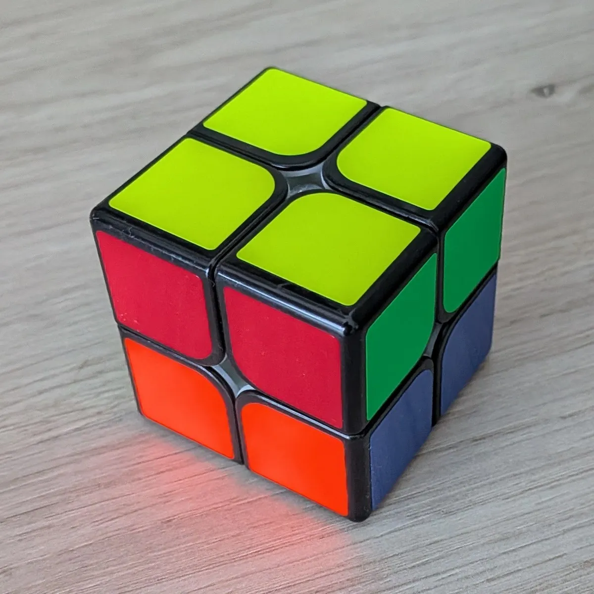 Un cubo de Rubik de 2x2 con la cara amarilla completa arriba y los laterales sin ordenar: dos cuadros rojos sobre dos naranjas a la izquierda y dos verdes sobre dos azules a la derecha