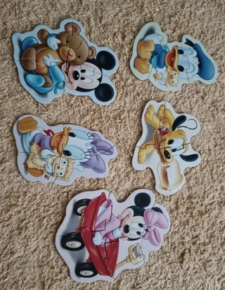 Cinco puzzles de Baby Mickey montados sobre una alfombra: Mickey con su osito, Donald, Daisy, Pluto y Minnie en un coche