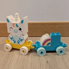 Un trenecito de LEGO Duplo con un vagón amarillo que lleva un unicornio y otro azul con un arcoíris