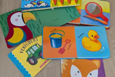 Varios libros de cartón para bebés abiertos en el suelo: uno de contar, uno con espejo, otro de vehículos y uno de texturas con un zorro