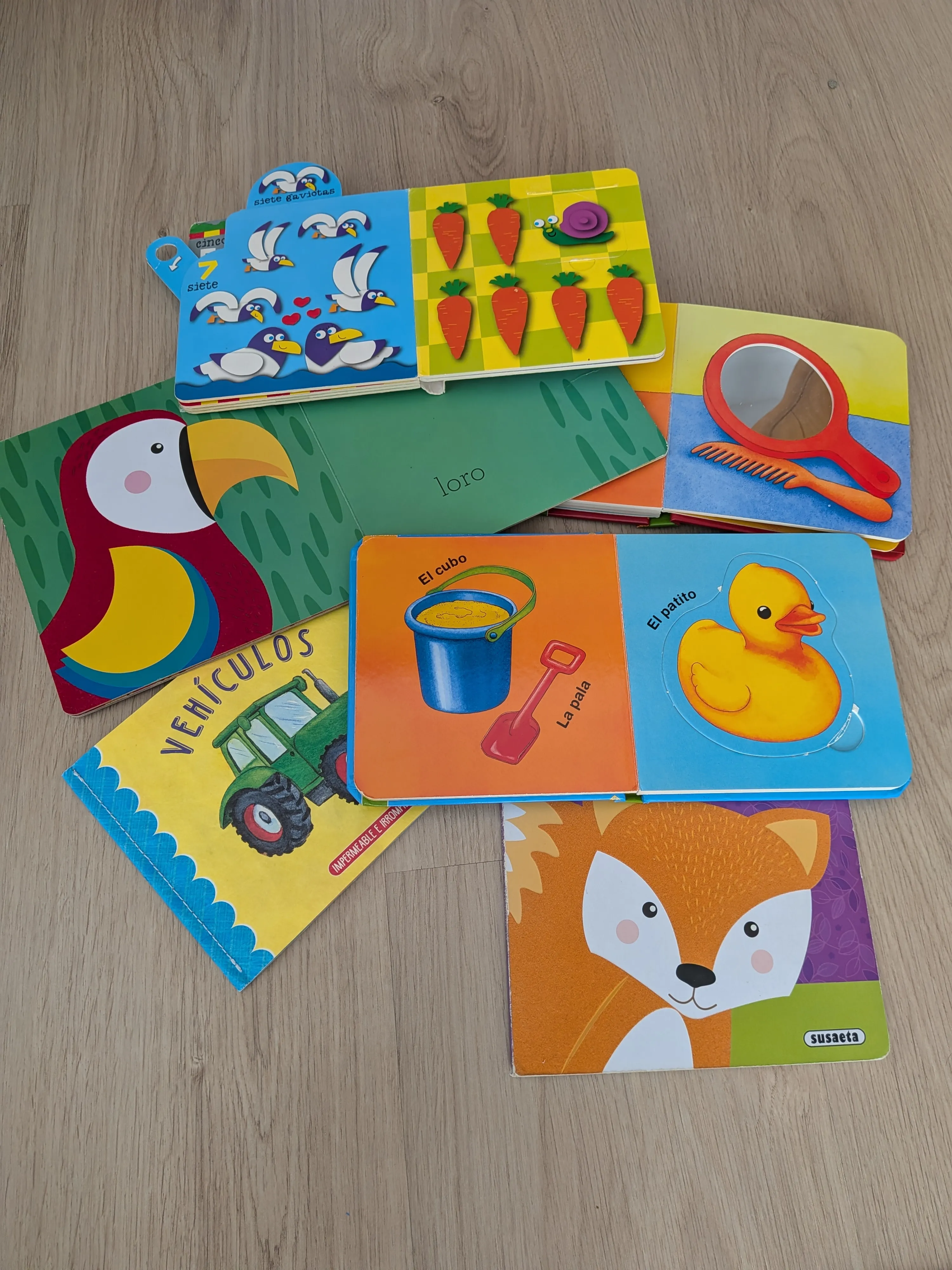 Varios libros de cartón para bebés abiertos en el suelo: uno de contar, uno con espejo, otro de vehículos y uno de texturas con un zorro