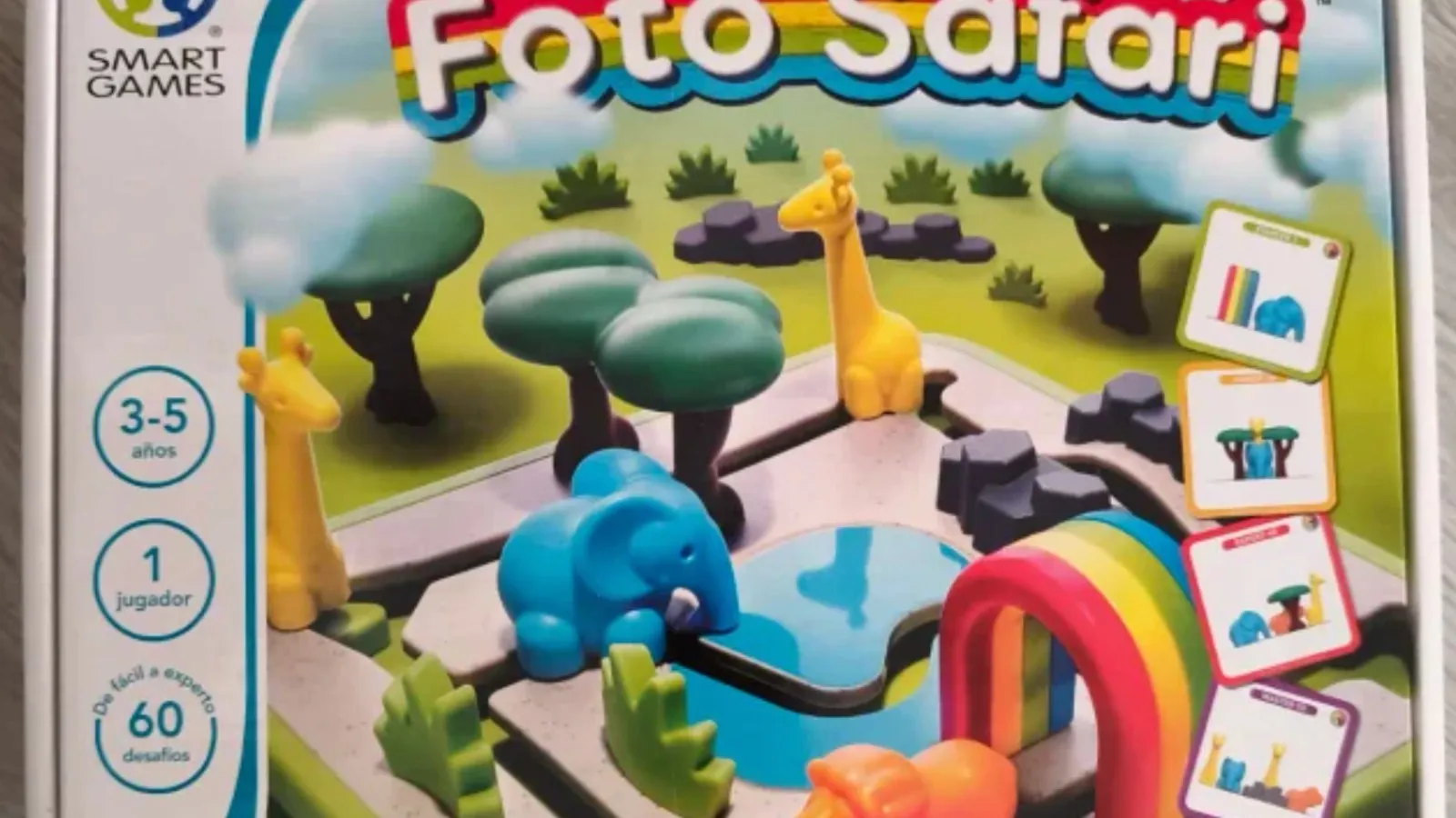 La caja de Foto Safari, con la jirafa, el elefante y el hipopótamo de plástico colocados entre árboles junto a un charco y un arcoíris