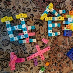 Varias figuras construidas con policubos de colores sobre una alfombra: una casa, una flor, una cruz y una equis