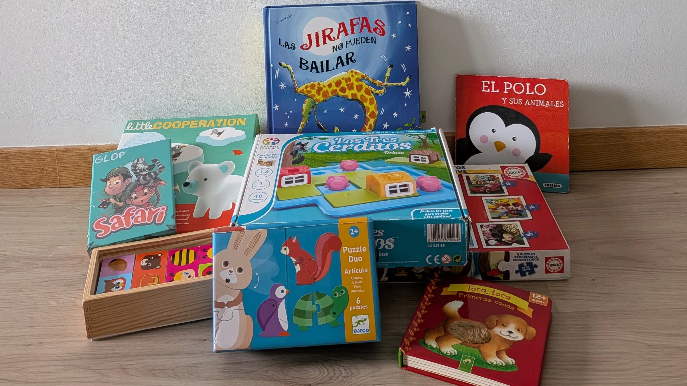 Juegos de mesa, puzzles y libros infantiles apilados en el suelo: Las jirafas no pueden bailar, Little Cooperation, Glop Safari, Los Tres Cerditos y varios libros de cartón