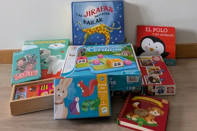 Juegos de mesa, puzzles y libros infantiles apilados en el suelo: Las jirafas no pueden bailar, Little Cooperation, Glop Safari, Los Tres Cerditos y varios libros de cartón