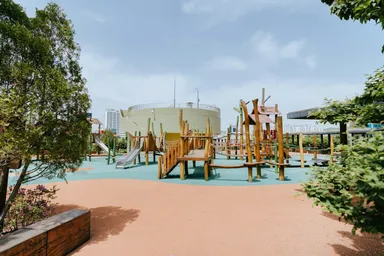 Parque infantil con estructuras de madera, toboganes y puentes de cuerda bajo un cielo azul