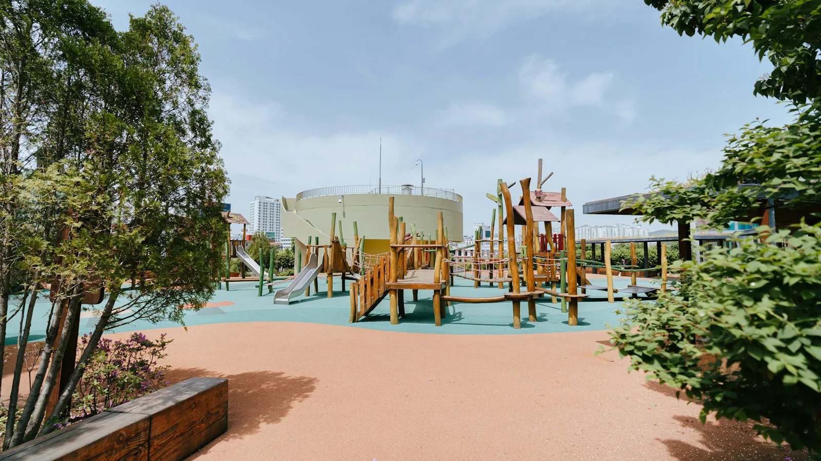 Parque infantil con estructuras de madera, toboganes y puentes de cuerda bajo un cielo azul