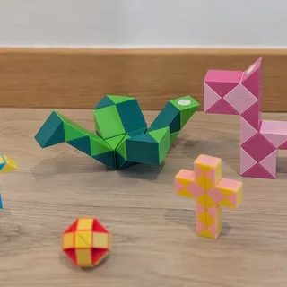 Varias serpientes mágicas montadas en figuras distintas sobre el suelo de madera: un pájaro verde, una pelota roja y una cruz rosa