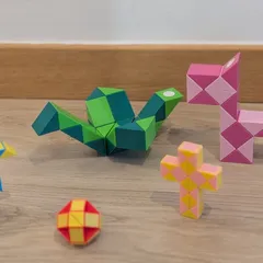 Varias serpientes mágicas montadas en figuras distintas sobre el suelo de madera: un pájaro verde, una pelota roja y una cruz rosa