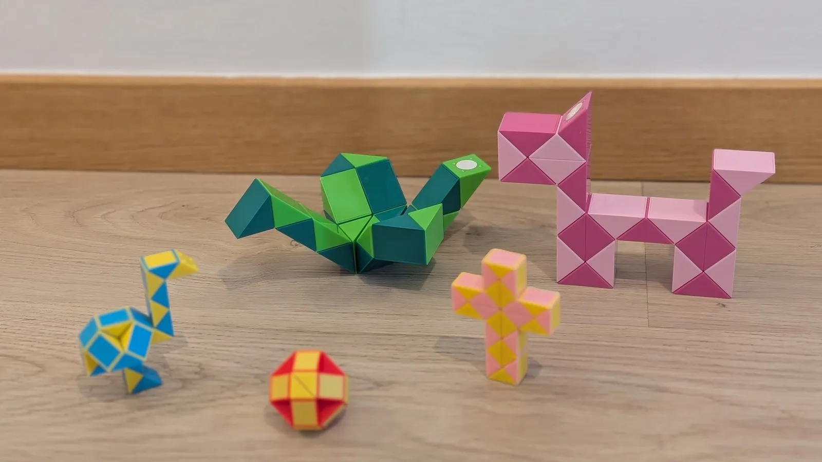 Cinco serpientes de Rubik montadas a la vez en el suelo: un avestruz azul y amarillo, un pájaro verde, una pelota roja, una cruz rosa y un perro rosa